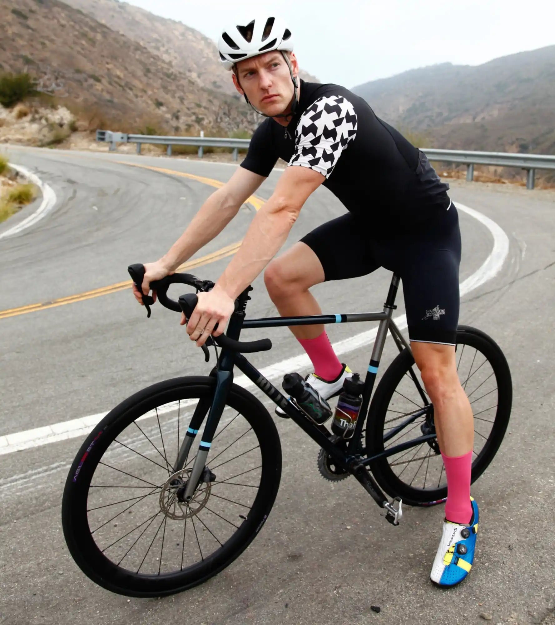 Black road bike with disc brakes and a cyclist wearing black and white cycling gear.