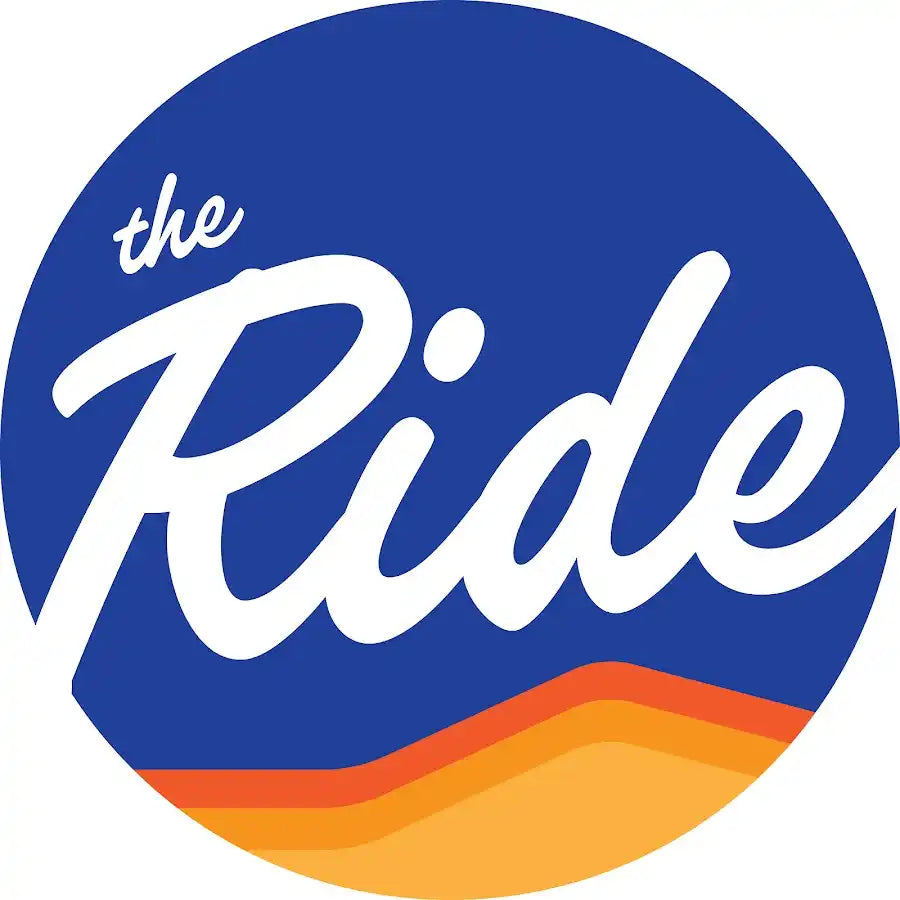 Circular blue logo with ’the Ride’ text and orange wavy lines at the bottom.