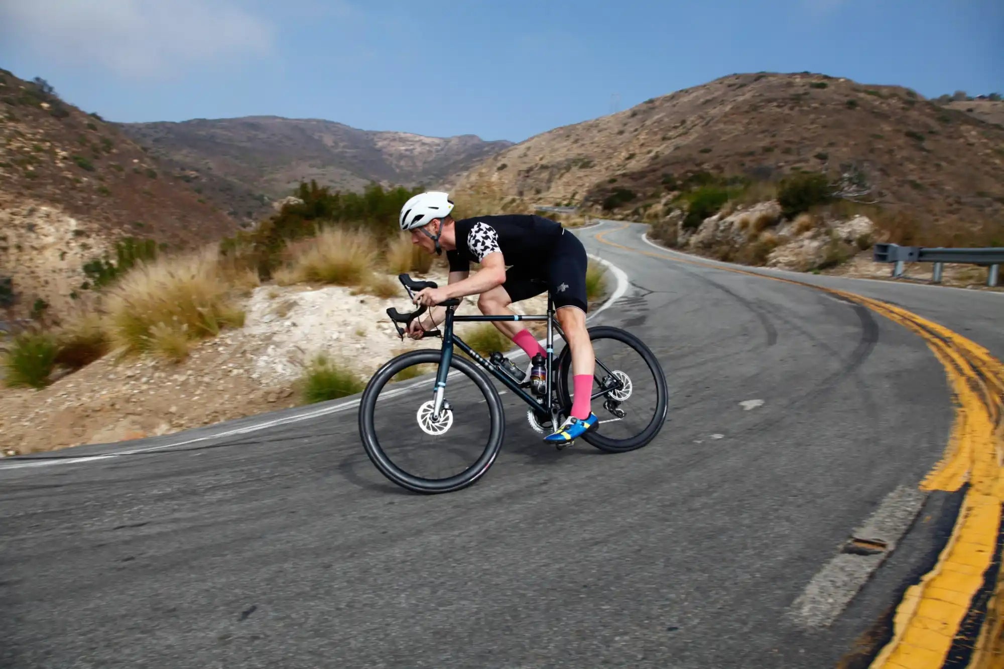 Cyclist in an aerodynamic position riding a racing bike on a curved mountain road.