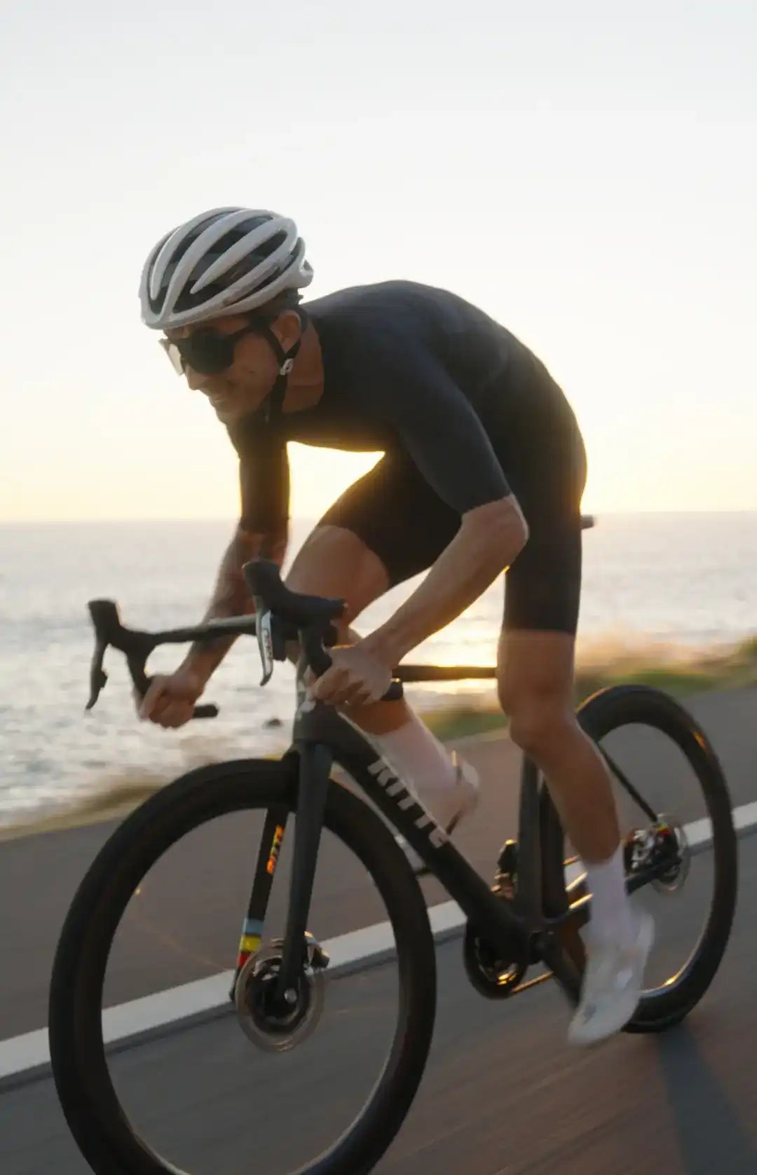 Cyclist in an aerodynamic position riding a Trek road bike at sunset.