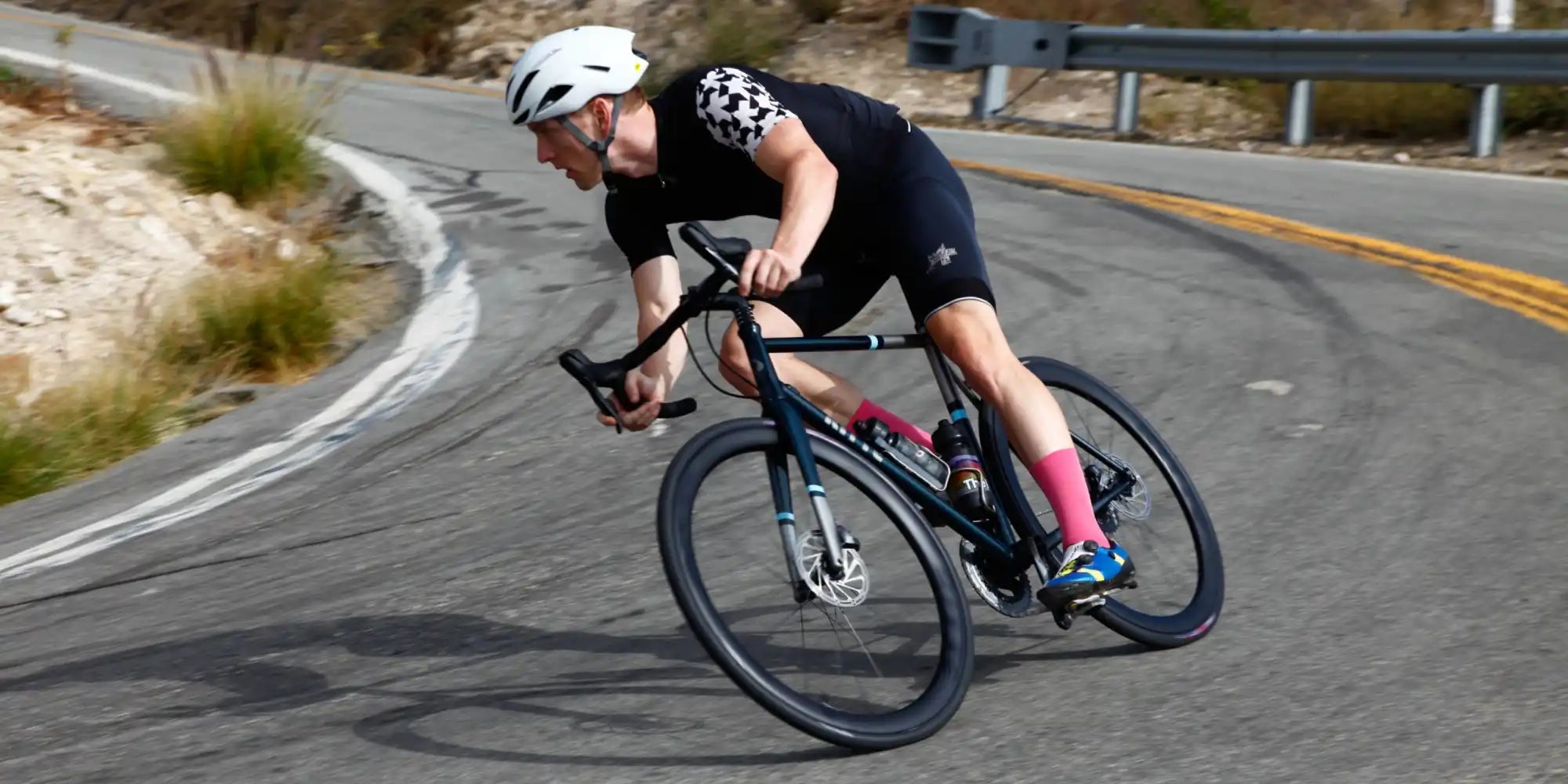 Cyclist in black attire leaning into a curve while riding a dark-colored road bike.