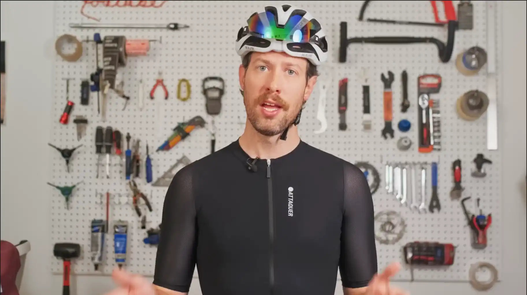 Cyclist wearing a black jersey and colorful helmet standing in front of a tool wall.