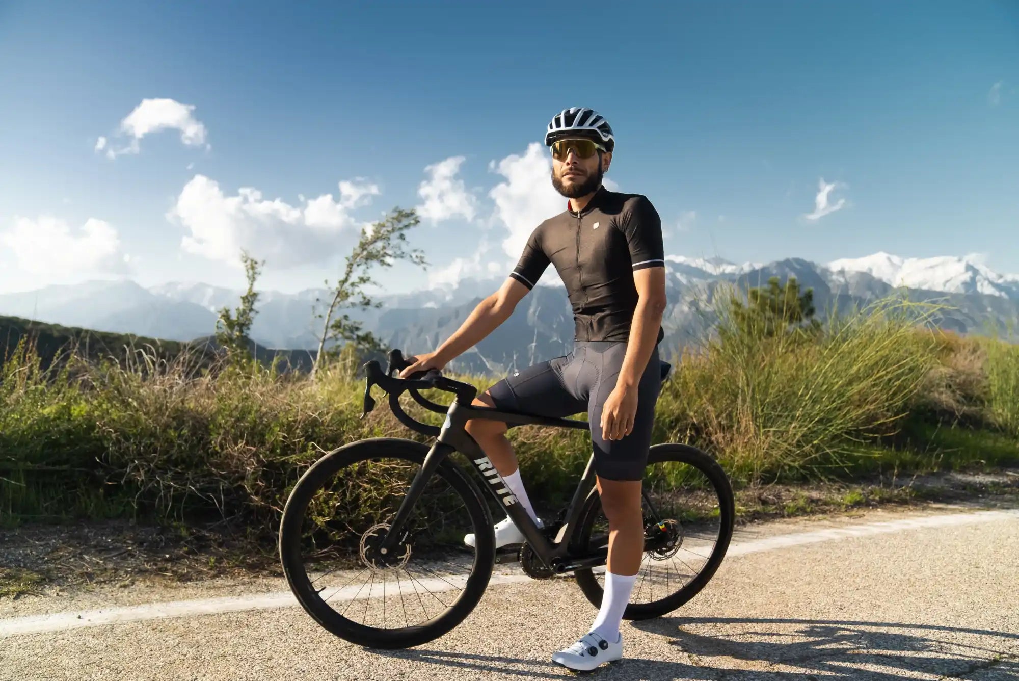 A cyclist in cycling gear standing with a black road bike.