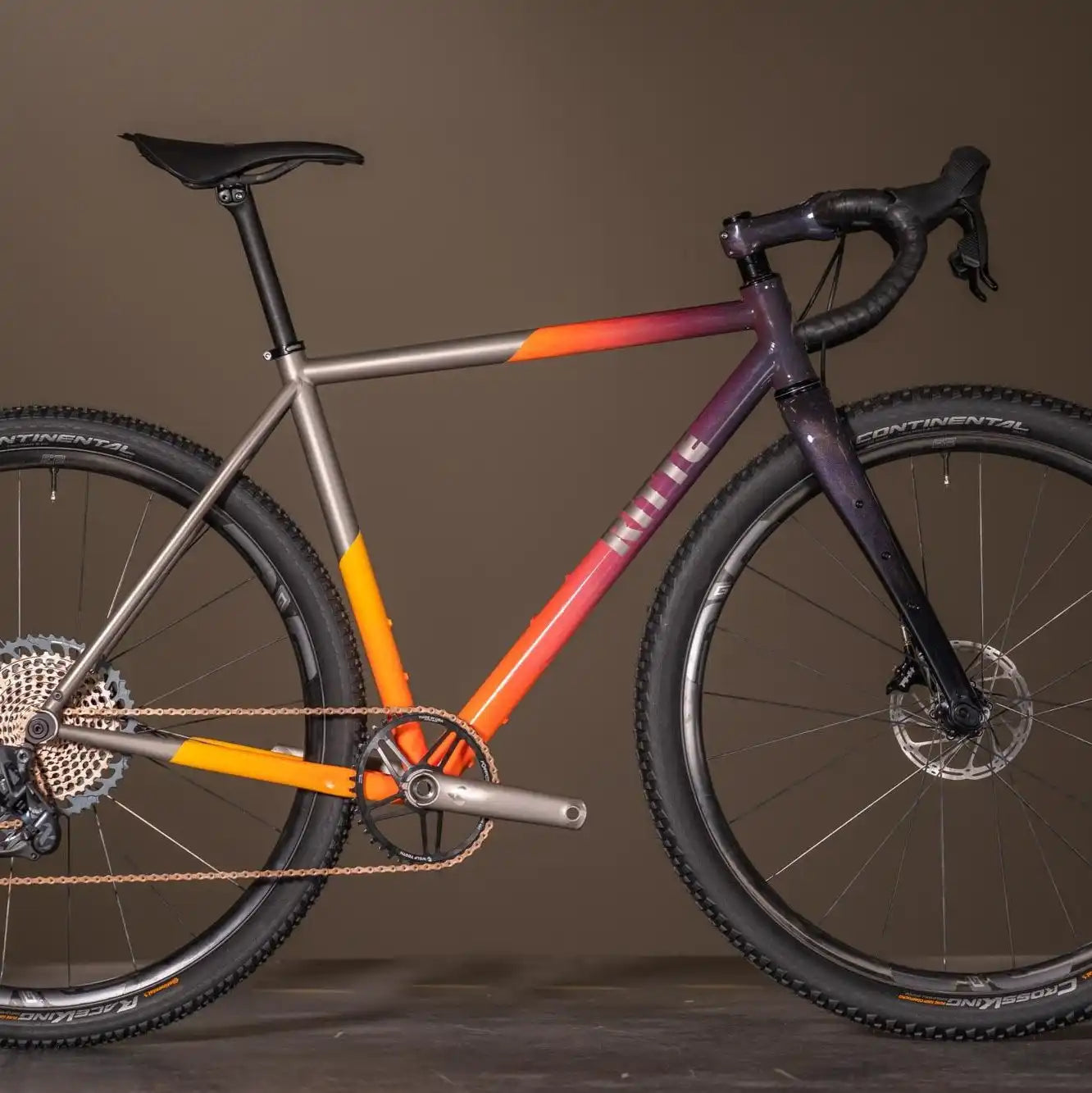 Gravel bicycle with a gradient paint scheme from silver to purple featuring orange accents.