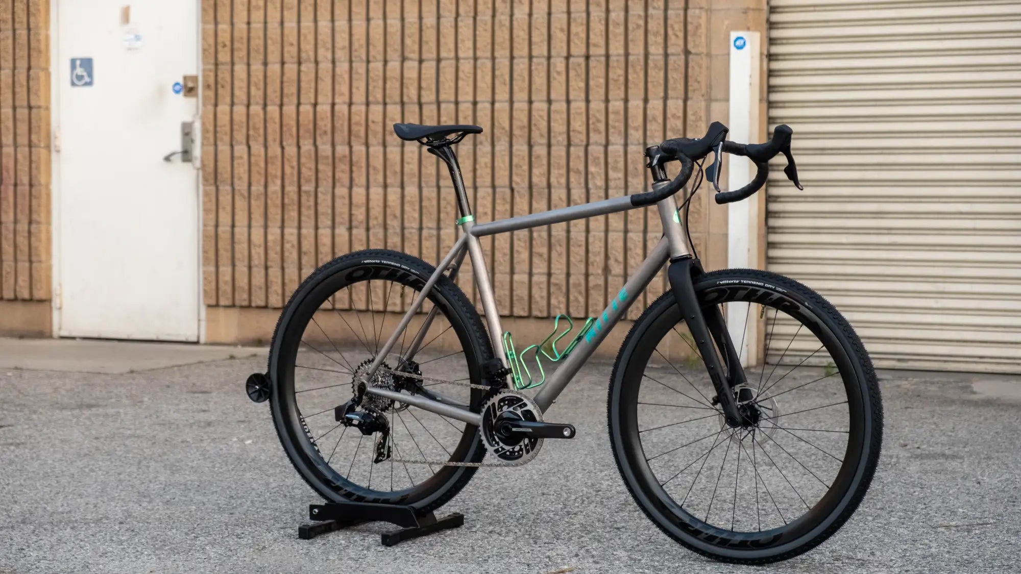 Gray gravel bike with black handlebars, seat, and tires, featuring a teal accent stripe along the frame.