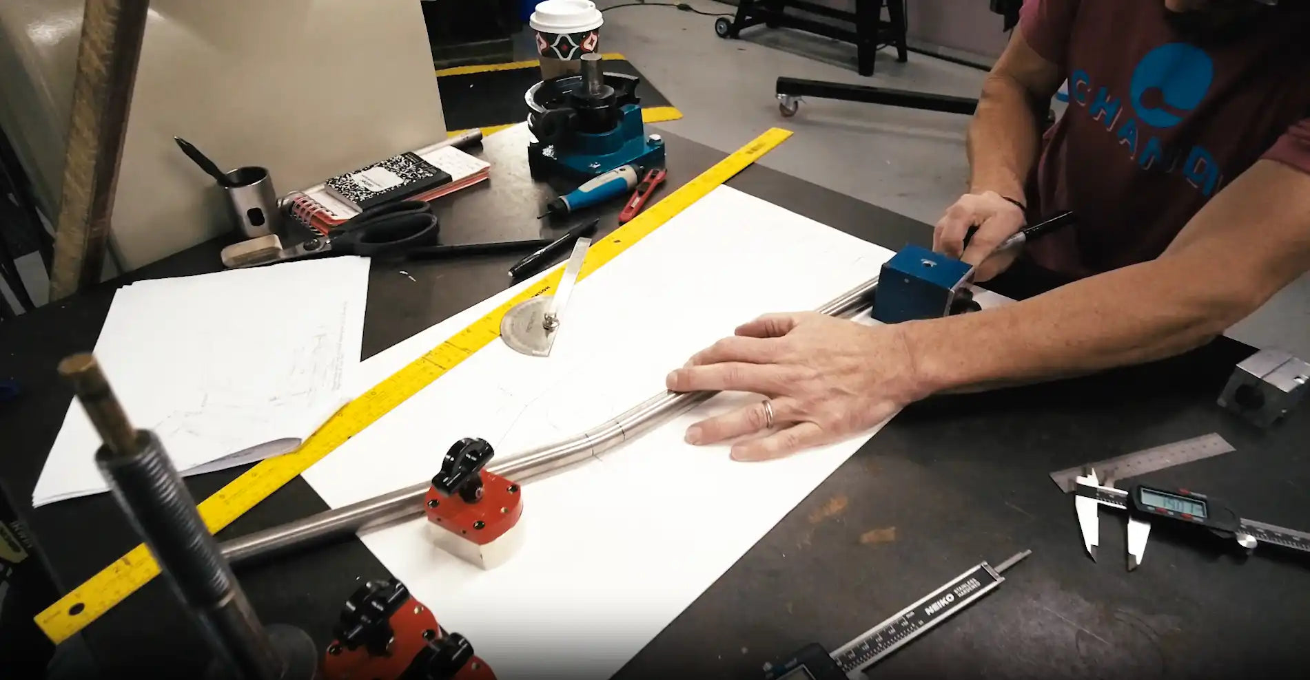 Hands working with measuring tools and papers on a workspace.