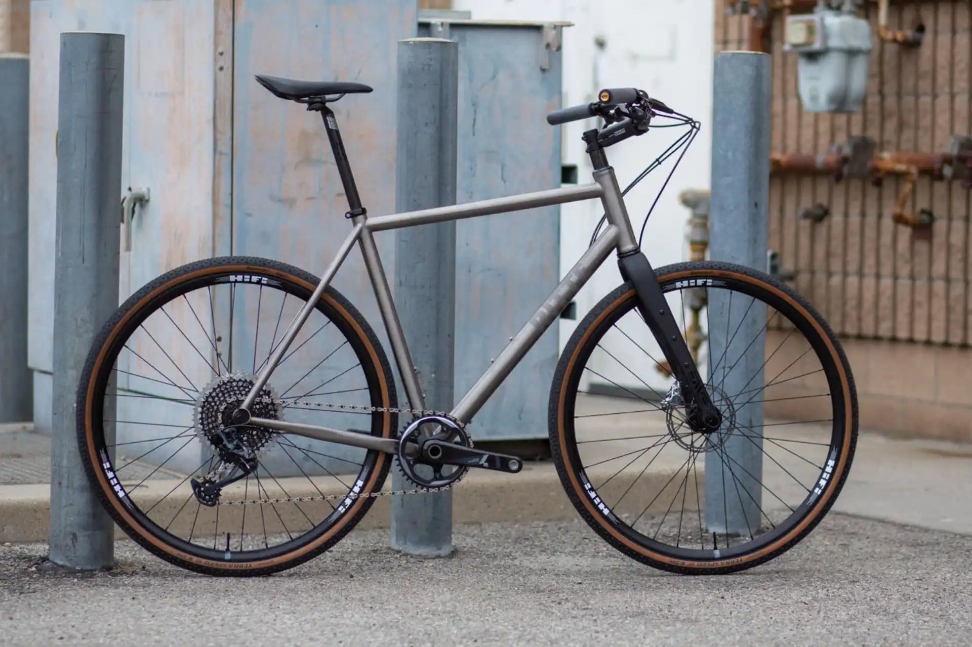 Modern titanium or steel flat-bar hybrid bicycle with disc brakes and brown tires.