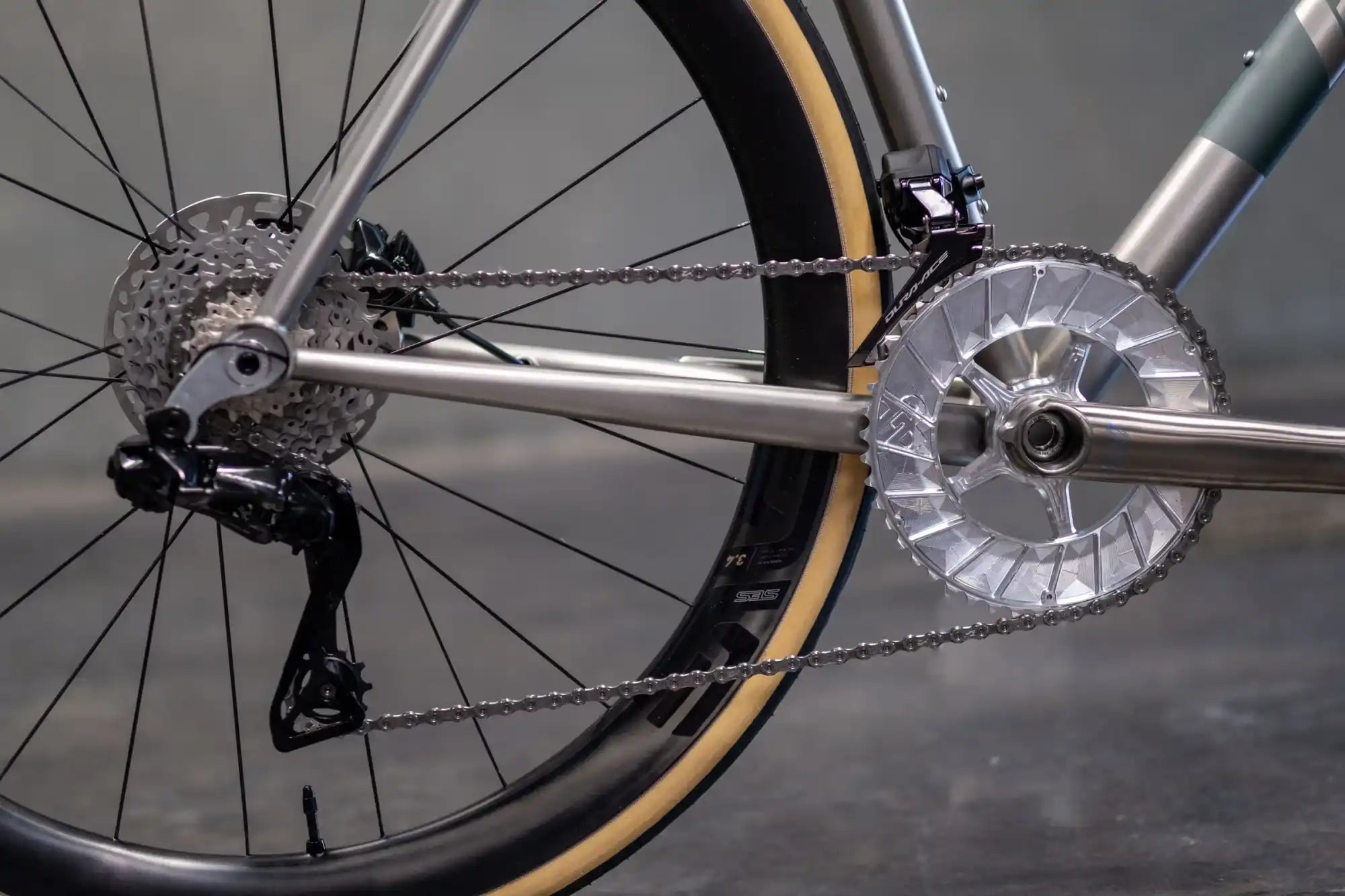 Bicycle drivetrain showing the chainring, cassette, and derailleur with a gum-wall tire visible.