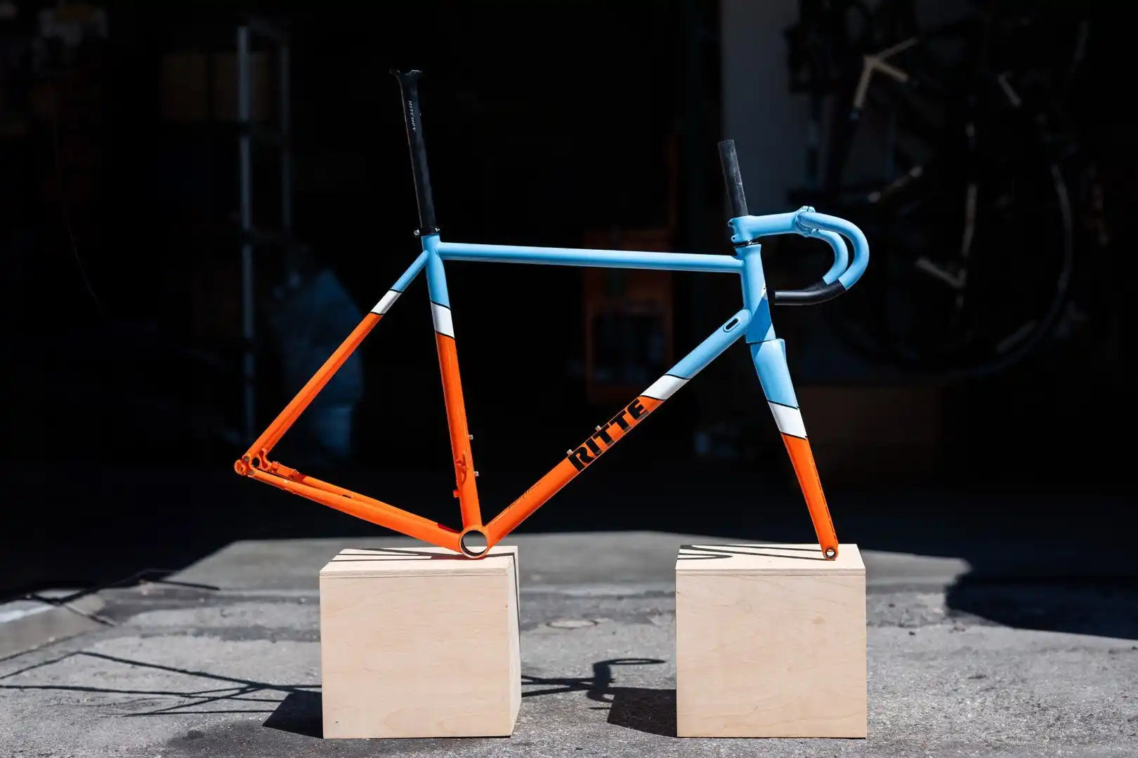 Bicycle frame painted in light blue and orange colors resting on two beige blocks.