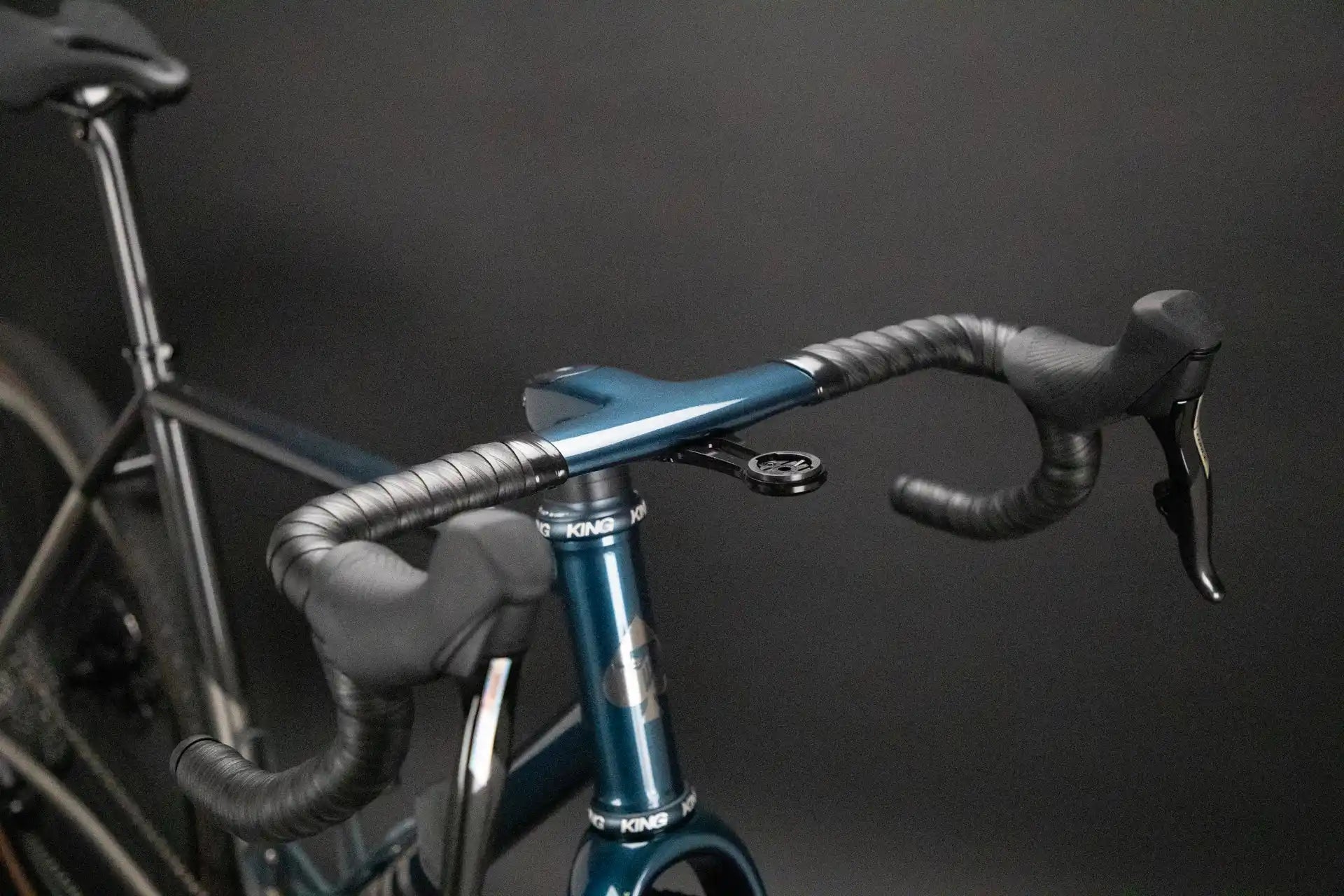 Racing bicycle handlebars wrapped in gray tape with a metallic blue stem.