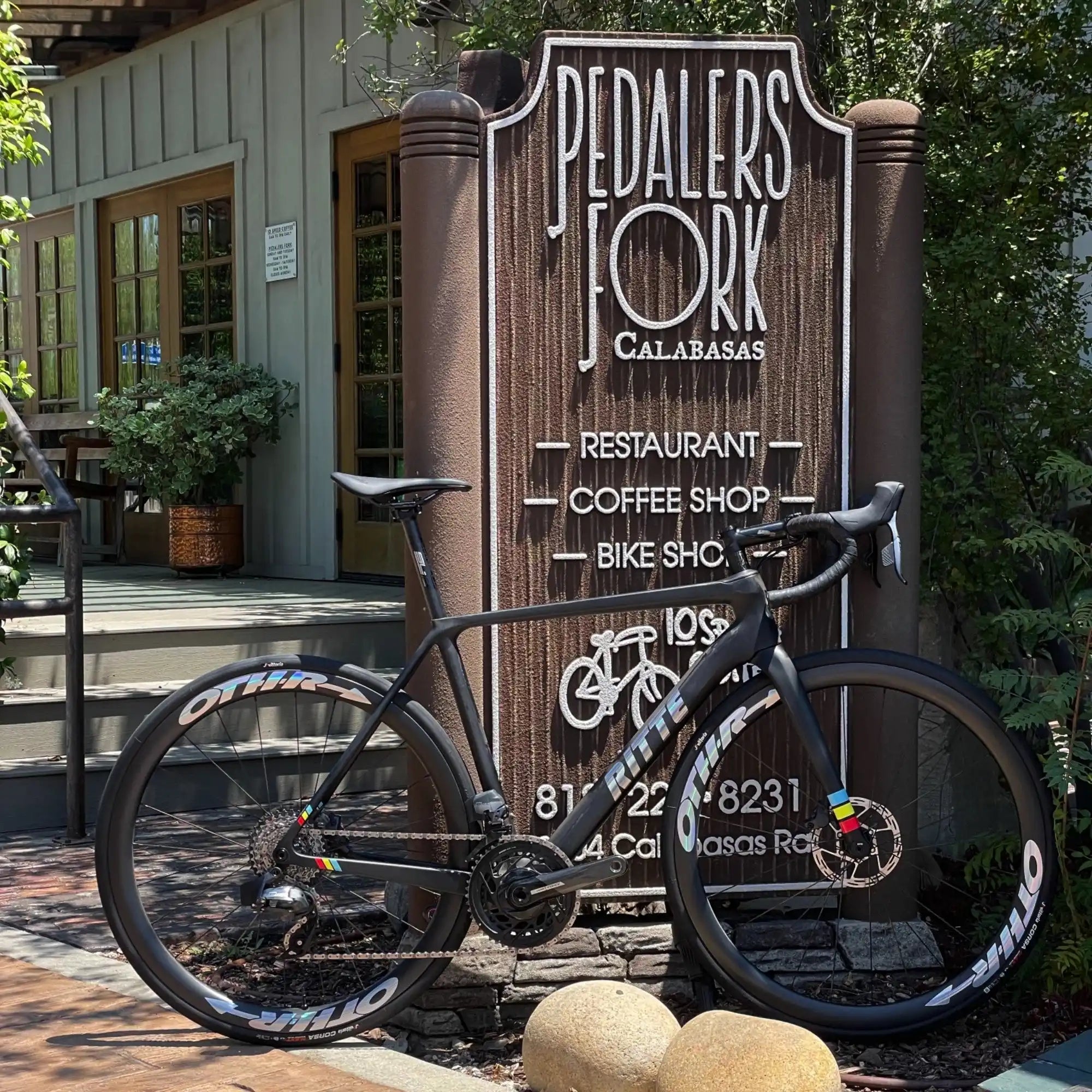 Black racing bicycle parked next to a wooden Pedalers Fork restaurant sign.