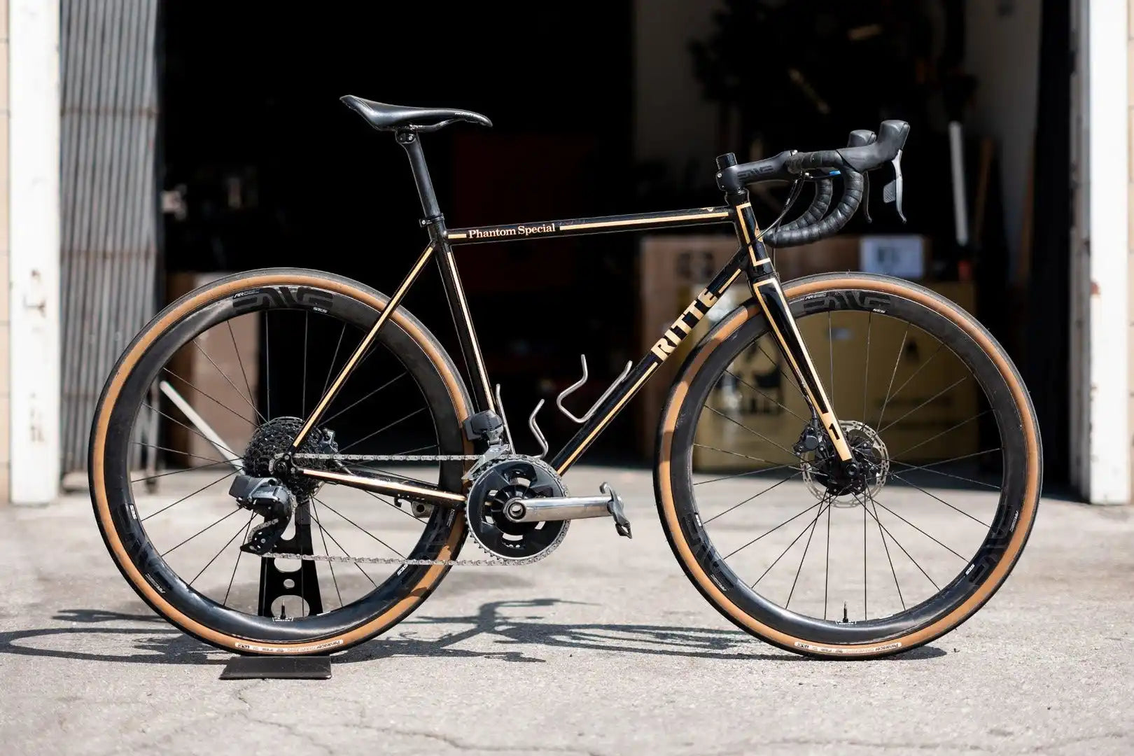 Black road bike with tan sidewall tires and disc brakes.