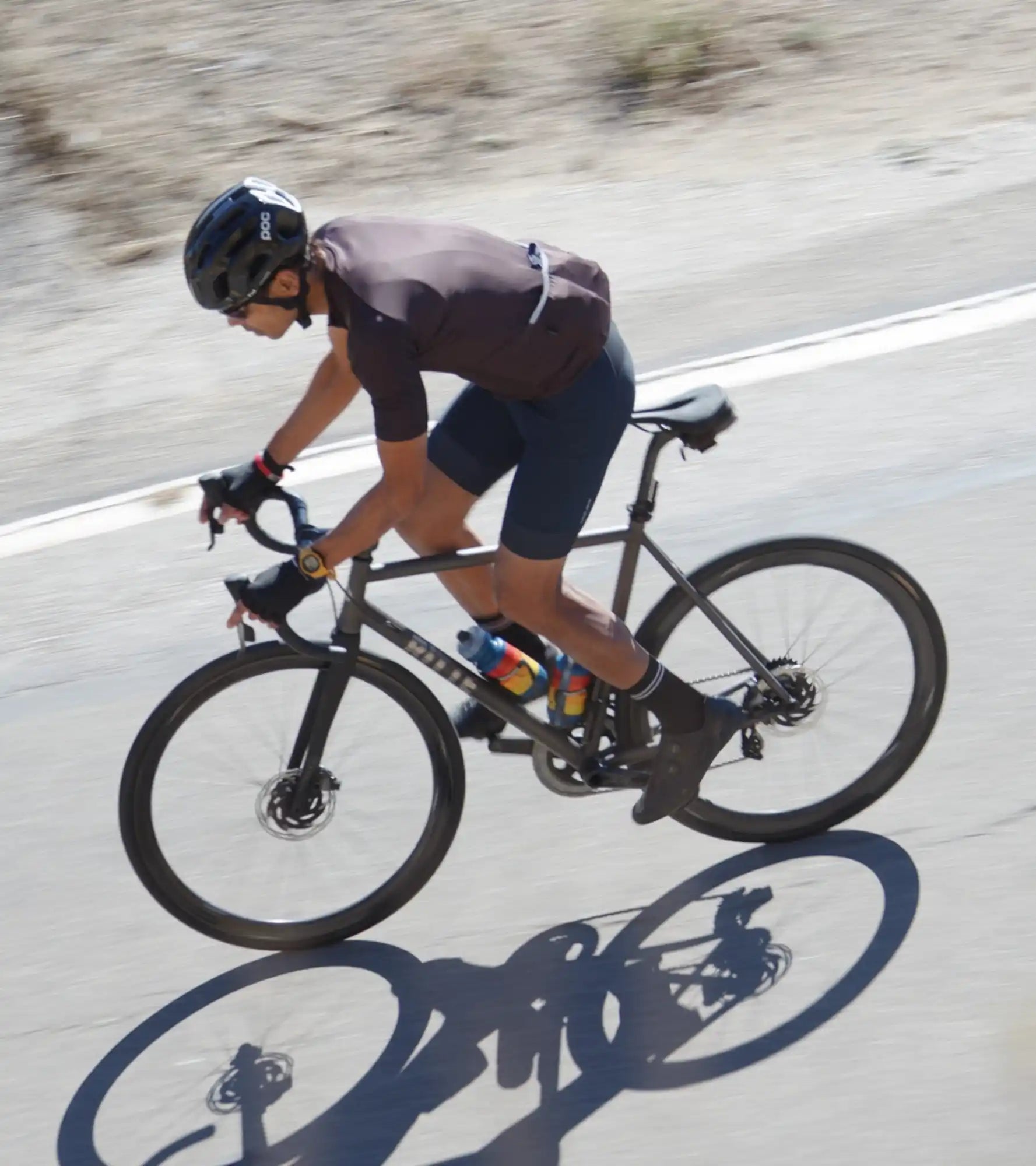 Cyclist riding a black road bike casting a shadow on the pavement.