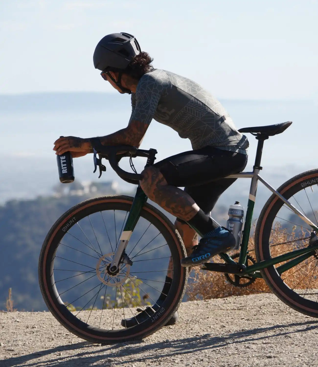 Cyclist riding a green gravel bike while holding a water bottle.