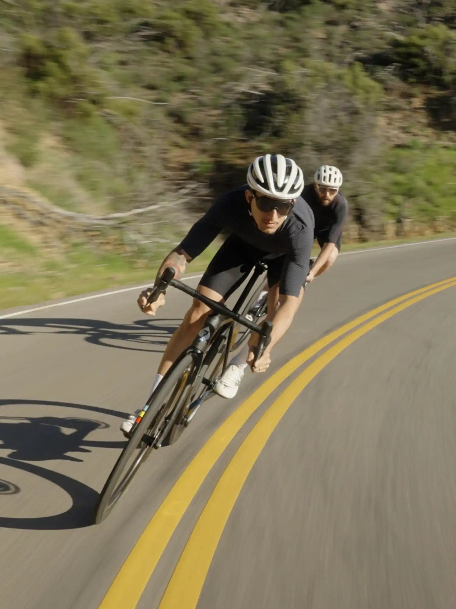 Cyclist in racing position on a road bike wearing black cycling gear and white helmet.