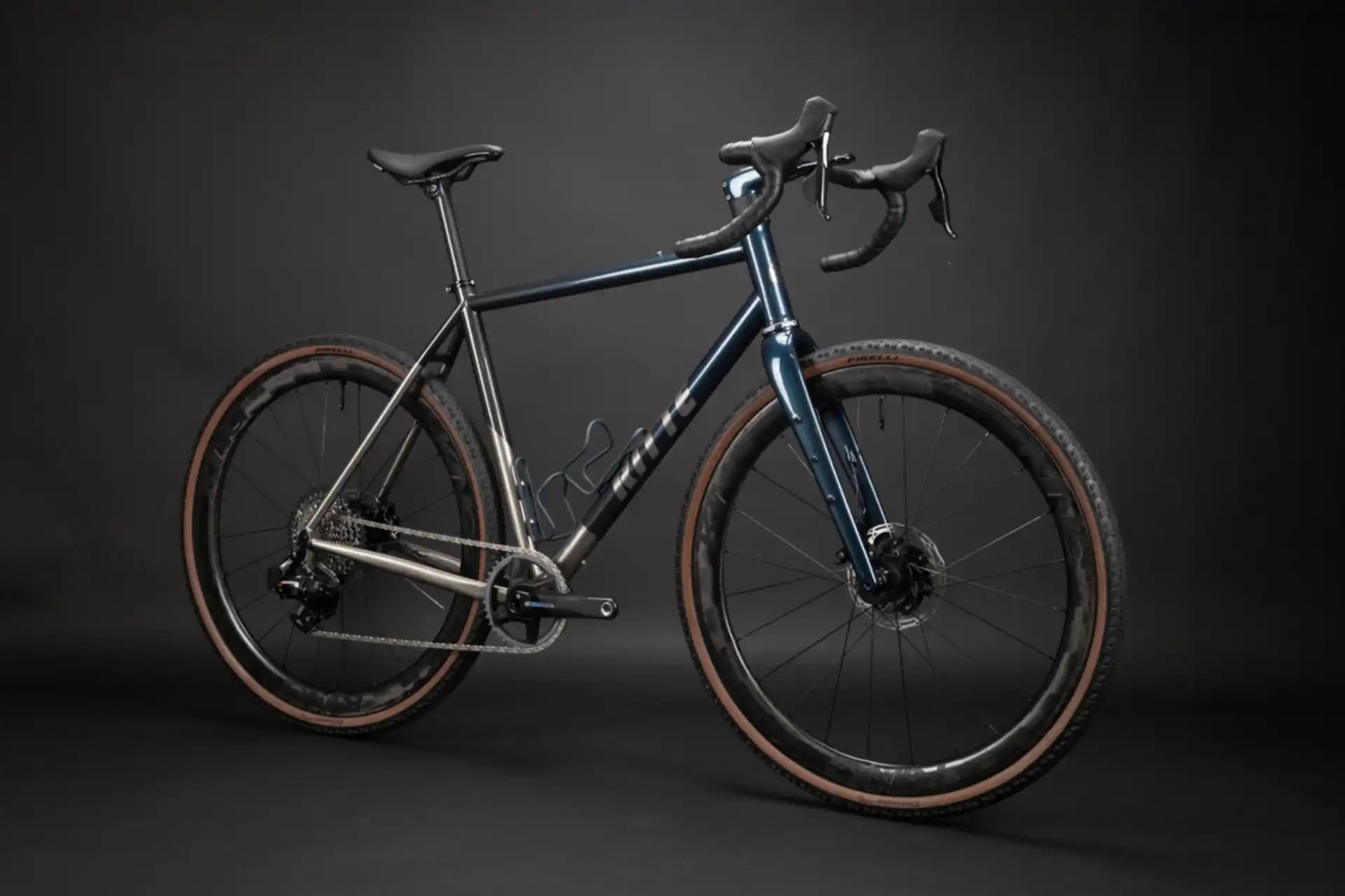 Dark metallic gravel bike with drop handlebars and brown tires.