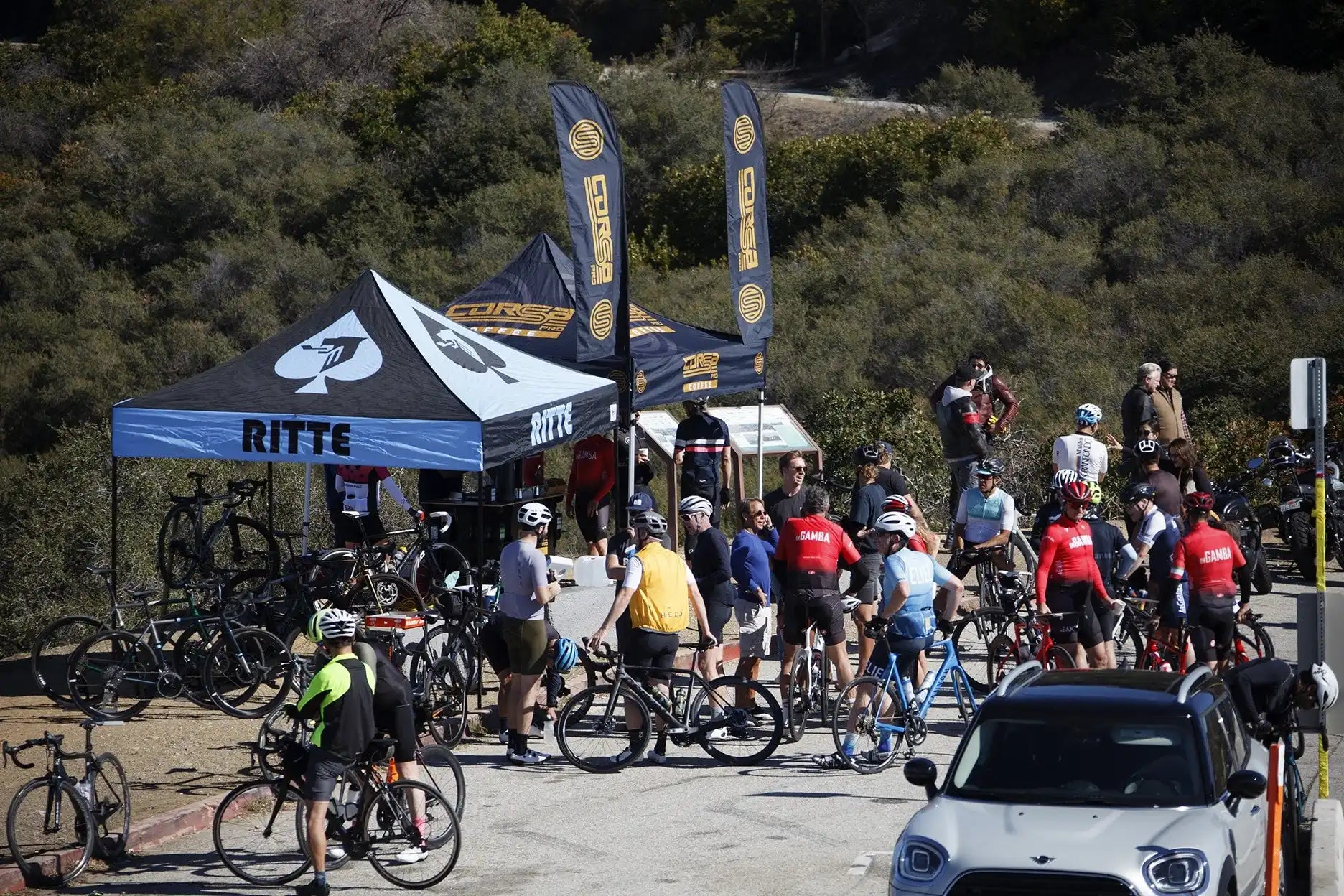 Group of cyclists gathered at a rest stop with vendor tents.