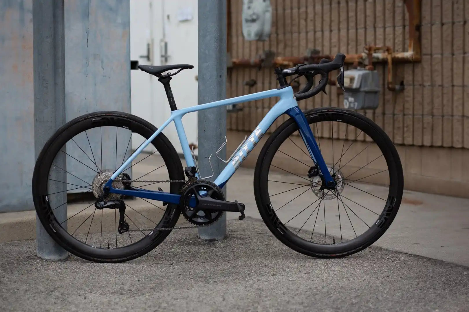 Light blue and navy road bike with disc brakes and drop handlebars.