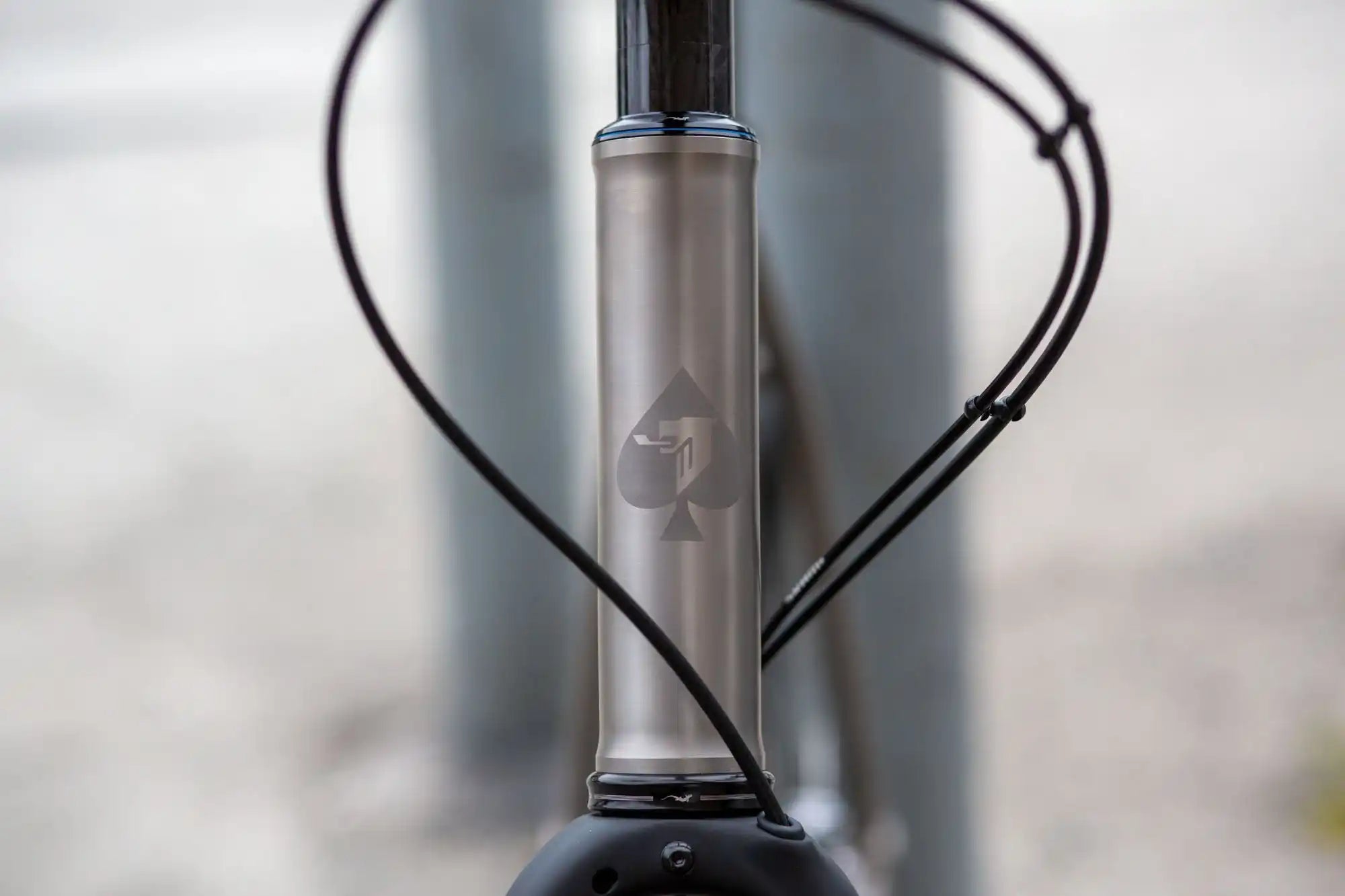 Metallic bicycle frame tube with a subtle logo etched on its surface.