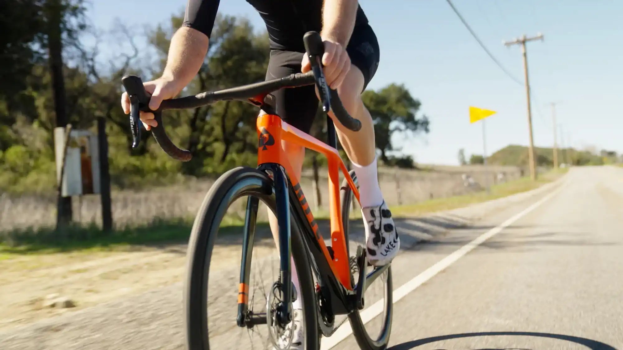 Orange road bike with black handlebars being ridden on pavement.