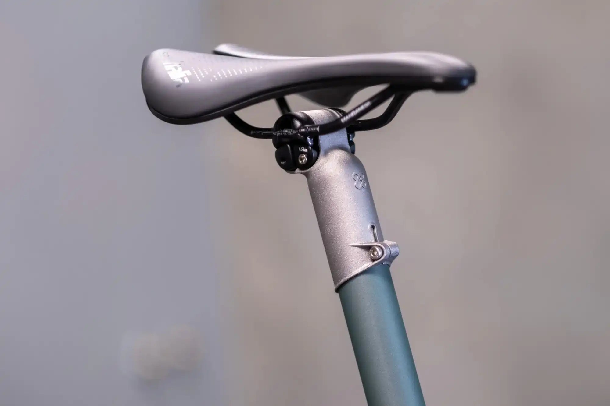 Silver bicycle seat and seatpost mounted on a blue-green frame.