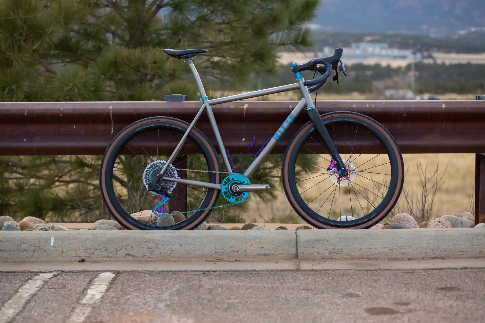 Turquoise and gray road bike with disc brakes leaning against a railing.